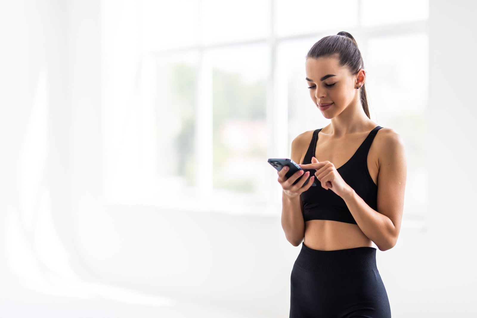 attractive healthy young woman with a fitness mat using mobile phone at the gym